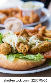 A fried oyster po-boy sandwich with cole slaw, french fries, and remoulade sauce