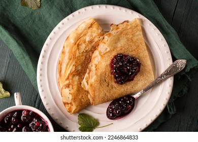 Fried pancakes with blackcurrant jam on a wooden table with a green napkin - Shutterstock ID 2246864833