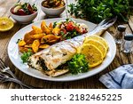 Fried perch with boiled potatoes, lemon and fresh vegetable salad served on wooden table 