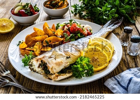 Fried perch with boiled potatoes, lemon and fresh vegetable salad served on wooden table 