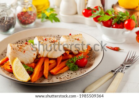 Fried pieces of cod loin, served with sweet potato fries. Light stone background. 