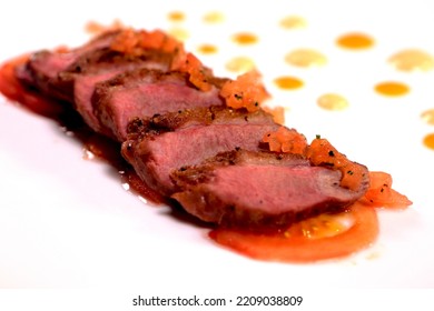 Fried Pieces Of A Meat With Sauce On A White Plate. Grilled Beef Steak Sliced On A White Plate. Medium Rare. Side View. 
