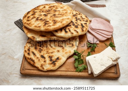 Fried pita bread stack on a wooden chopping board with ham slices and goat cheese, home made meal concept