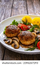 Fried pork meatballs with boiled potatoes and fried mushrooms on wooden table  - Shutterstock ID 2396267293