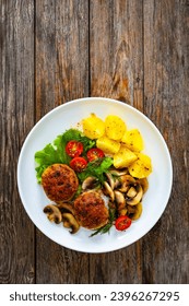 Fried pork meatballs with boiled potatoes and fried mushrooms on wooden table  - Shutterstock ID 2396267295