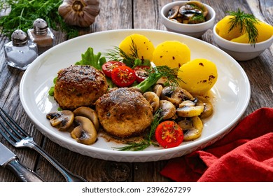 Fried pork meatballs with boiled potatoes and fried mushrooms on wooden table  - Shutterstock ID 2396267299