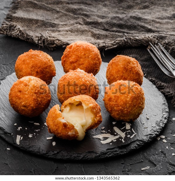 Fried\
potato cheese balls or croquettes with spices on black plate over\
dark stone background. Unhealthy food, top\
view