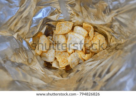 Fried potato golden chips with hot red pepper on bottom of the foil packaging. Texture. Background