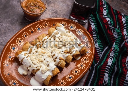 Fried potato tacos with cream and cheese in a Mexican mud dish. Tacos dorados, Mexican food.