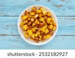 Fried potatoes on white plate over blue wooden background. Top view.