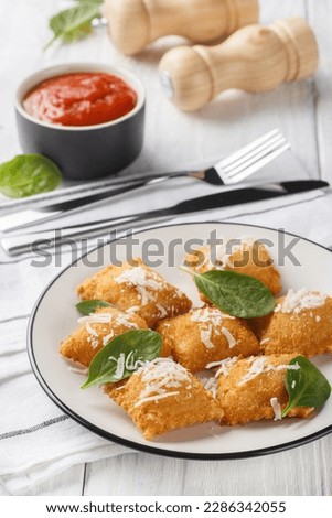 Fried ravioli is breaded and deep-fried pasta stuffed with soft cheese and spinach served with marinara sauce for dipping closeup on the wooden table. Vertical

