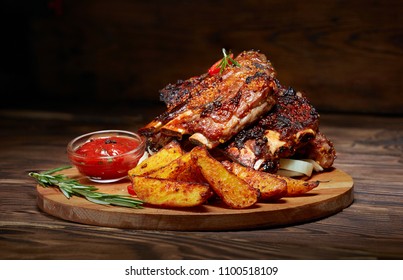 Fried ribs with rosemary, potatoes rustic, onion, sauce on wooden round Board. Dark background. Place for text, copyspace