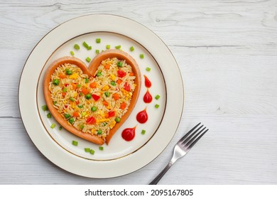 Fried rice with carrots,onions,tomatoes,green peas,spring onions,eggs and soy sauce in heart shaped sausage on plate with wooden background.Healthy food idea for Valentine's day.Top view.Copy space

