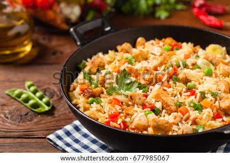 Fried rice with chicken. Prepared and served in a wok. Natural wood in the background. Front view.