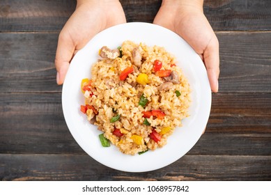 Fried Rice With Vegetables And Pork Holding By Hand On Wooden, Top View