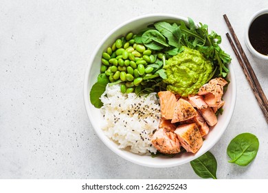 Fried salmon salad with rice, edamame and guacamole, top view. Cooked salmon poke bowl. Healthy diet recipe concept.