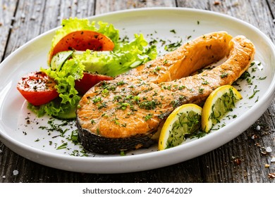Fried salmon steak and fresh vegetable salad served on wooden table 