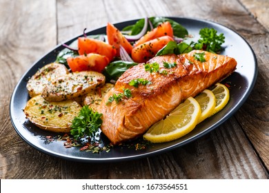 Fried salmon steak with potatoes and vegetables on wooden table