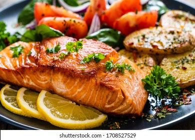 Fried salmon steak with potatoes and vegetables on wooden table - Shutterstock ID 1708527529