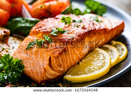 Fried salmon steak with potatoes and vegetables on wooden table