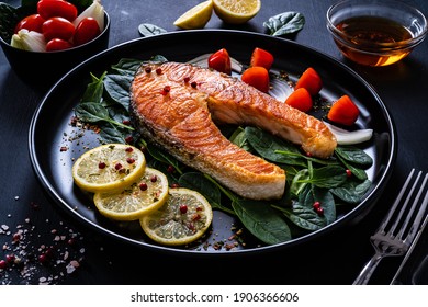 Fried salmon steak with spinach, lemon and cherry tomatoes served on black plate on wooden table 