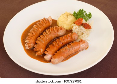 Fried sausage with sauce,boiled 
 boiled potato, dry tomatoes and parsley on white dish.