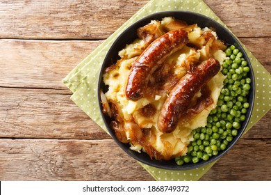 Fried sausages with mashed potatoes, onion gravy and green peas close-up in a plate on the table. horizontal top view from above
