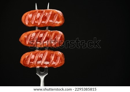 Fried sausages on fork, black background. Place for text