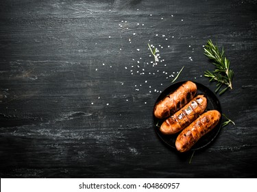 Fried sausages in a pan with rosemary . On the black Board.
