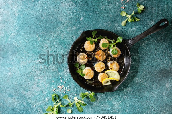 Fried scallops with butter lemon spicy sauce in\
cast-iron pan served with green salad over turquoise texture\
background. Top view, copy\
space