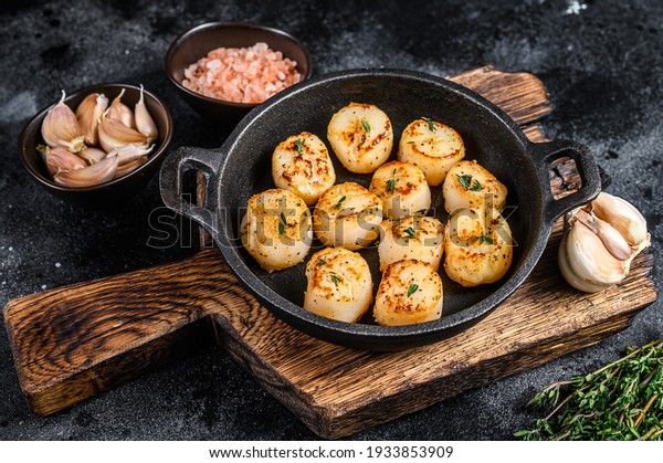Fried scallops with butter sauce in a pan. Black\
background. Top view.