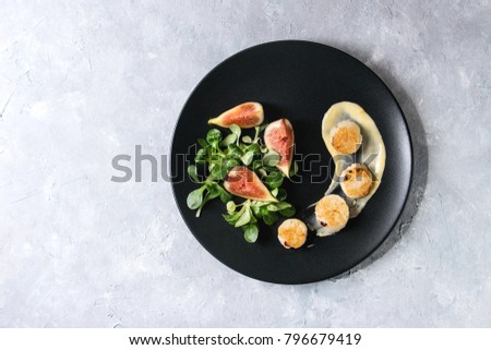 Fried scallops with lemon, figs, sauce and green salad served on black plate over gray texture background. Top view, copy space. Plating, fine dining