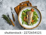 Fried sea bass fillet with vegetable salad, Dicentrarchus fish. Gray background. Top view.
