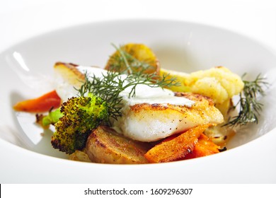 Fried Sea Cod Fillet With Baked Vegetables On White Restaurant Plate Isolated. Delicious Breaded Atlantic Codfish Filet With Fried Broccoli, Potatoes And Garnished With Fresh Dill Closeup