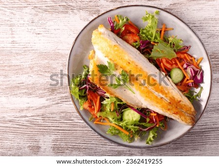 Fried seabass fish fillet over salad