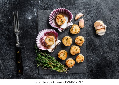 Fried seafood scallops meat with butter in a shells. Black background. Top view.