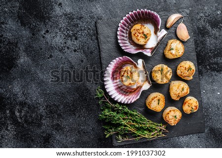 Fried seafood scallops meat with butter in a shells. Black background. Top view. Copy space