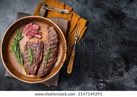Fried sirloin flap or flank beef steak with herbs in a wooden plate. Black background. Top view. Copy space.