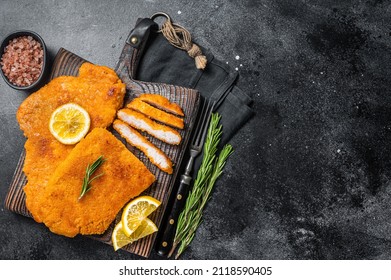 Fried sliced weiner schnitzel on a wooden board with herbs. Black background. Top view. Copy space