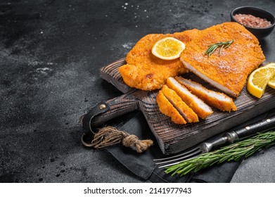 Fried sliced weiner schnitzel on a wooden board with herbs. Black background. Top view. Copy space.