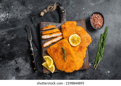 Fried sliced weiner schnitzel on a wooden board with herbs. Black background. Top view.