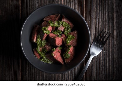 Fried slices of beef tenderloin in pesto sauce in a deep plate on a wooden table.