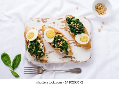 Fried Spinach, Egg And Pine Nuts Sandwiches Or Bruschetta On Light Background. Delicious Healthy Breakfast Or Snack. Top View.