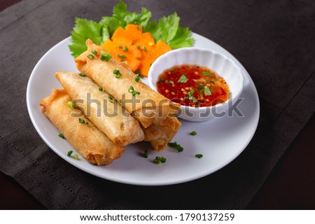 Fried spring rolls on a white plate and spicy sauce