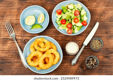 Fried squid rings breaded with fresh vegan salad on rustic wooden table. - Powered by Shutterstock