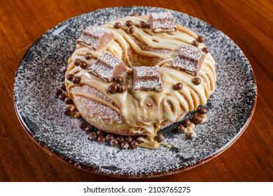 Fried staple garnished with white chocolate, milk chocolate pralines, kinder chocolate bar and icing sugar served on a black plate