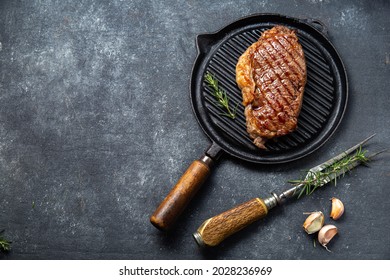 Fried Strip Loin Steak On Vintage Cast Iron Grill Pan And Cutlery Set, Black Background. Top View