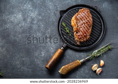 Fried strip loin steak on vintage cast iron grill pan and cutlery set, black background. Top view