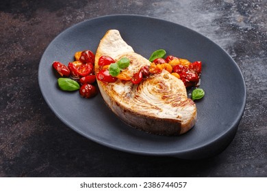 Fried swordfish steak with tomatoes and paprika served as close-up on a design plate 
