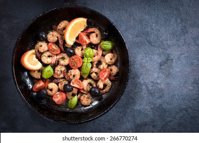 Fried tiger shrimps with ingredients in the pan from above on dark background with blank space
